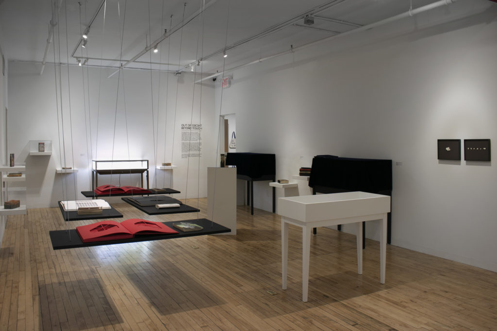 a dark gallery with books displayed on hanging tables with dramatic lighting